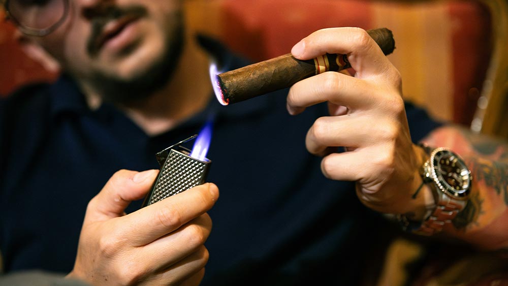 Barbat care isi aprinde un trabuc cu o bricheta cu arzator