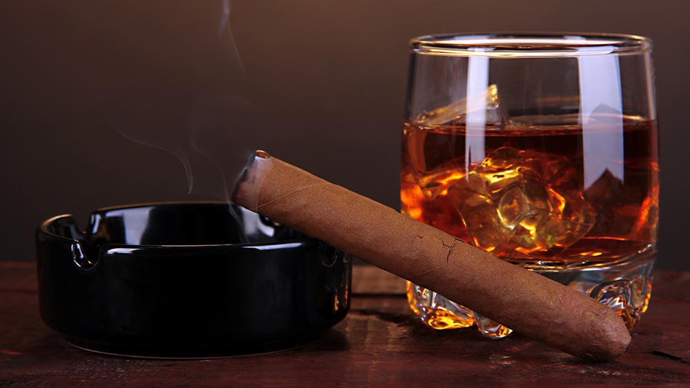 Un trabuc pe o scrumiera langa un pahar de bautura